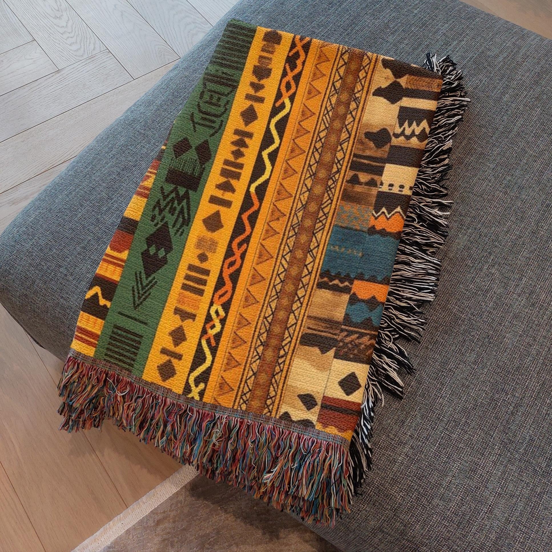 Kök Stüdyo woven throw blanket with Ndebele-inspired geometric patterns in green, yellow, orange, and blue. Features fringe detail.
