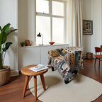 Kök Stüdyo Ndebele-inspired woven throw blanket with geometric patterns in tan, blue, and rust on an armchair.