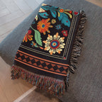 Kök Stüdyo black woven blanket with vibrant floral pattern, featuring Ojibwe-inspired art, fringed edges, and a geometric border.